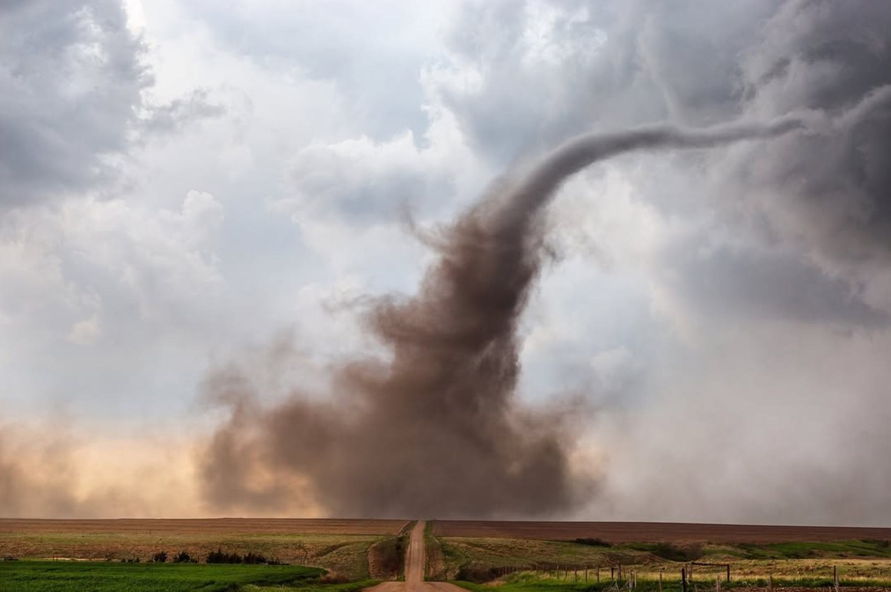 A rope tornado kicking up a dust cloud over open farmland, with a dirt road leading toward it