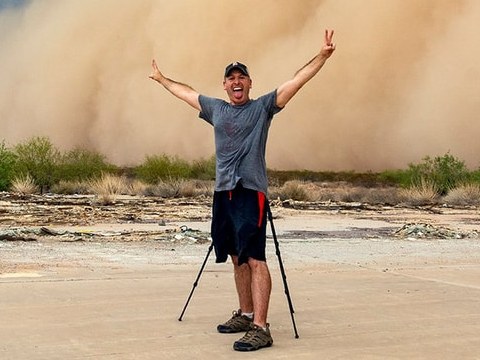 John Sirlin, arms raised, in front of a towering haboob